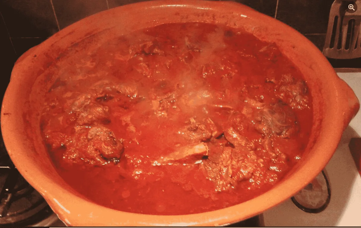 Agnello al sugo alla siciliana in casseruola di terracotta con salsa di pomodoro e alloro