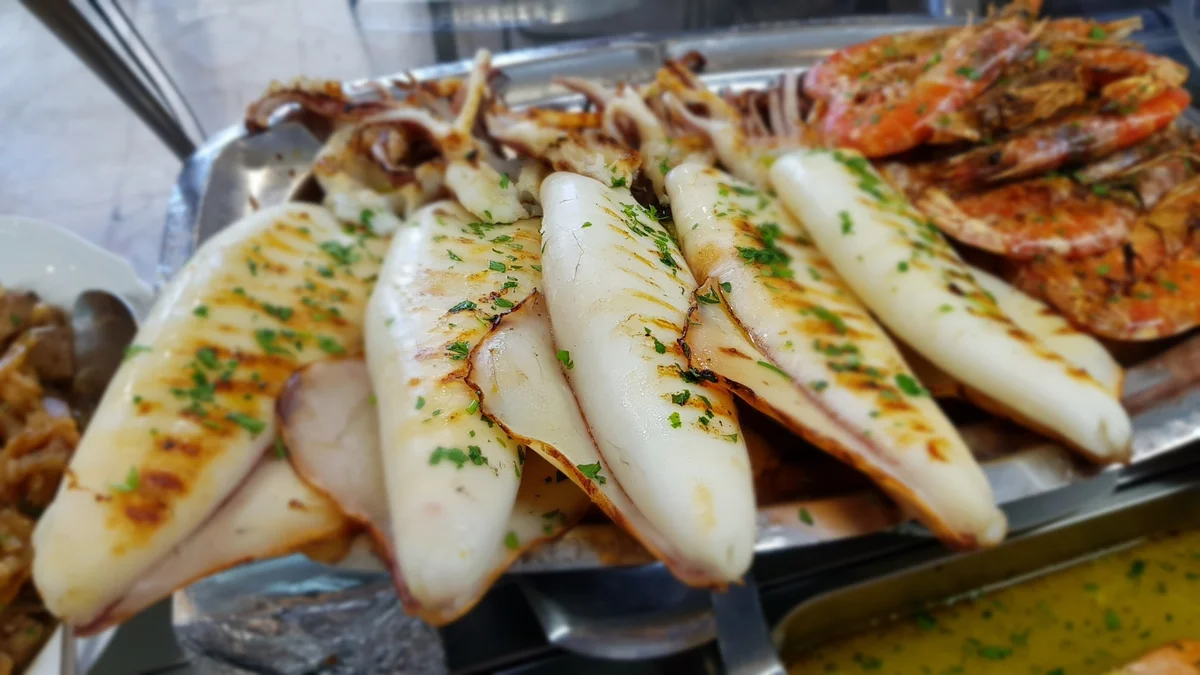 Calamari arrosto alla griglia con salmoriglio e fette di limone su piatto in ceramica siciliana