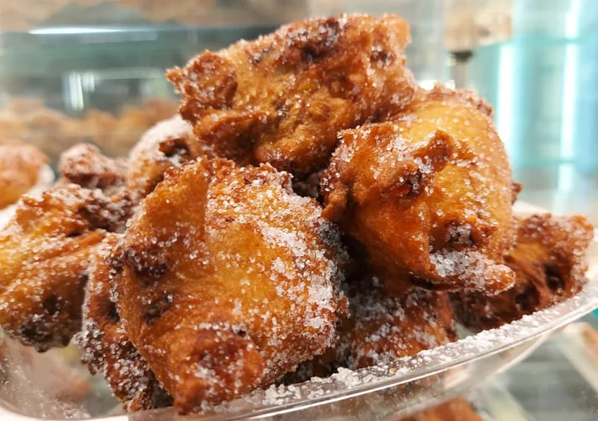 Frittelle con uvetta e semi di finocchio dorate e spolverate di zucchero su piatto di ceramica siciliana