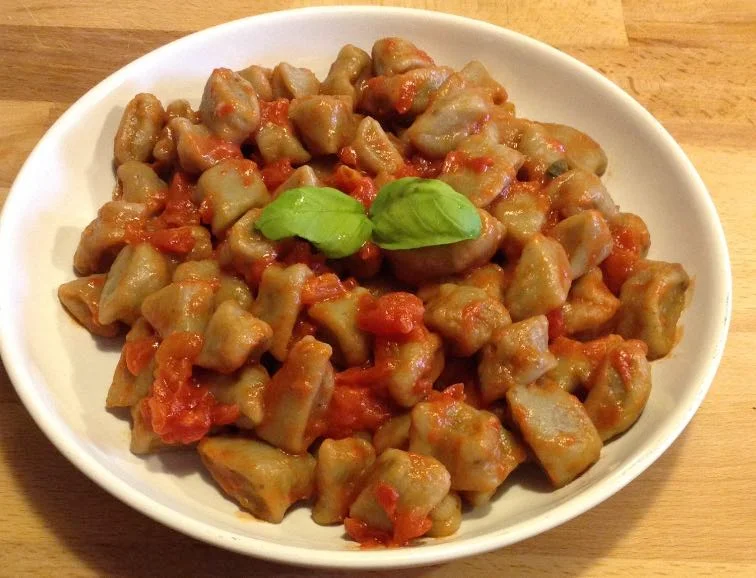 Gnocchi di melanzane con sugo di pomodorini serviti su piatto in ceramica siciliana decorata
