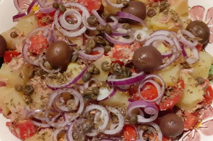 Insalata pantesca con patate, pomodori, olive e capperi in ciotola di ceramica colorata