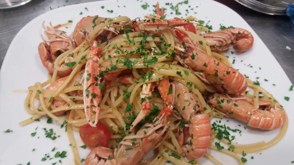 Linguine agli scampi con pomodorini e prezzemolo su piatto siciliano