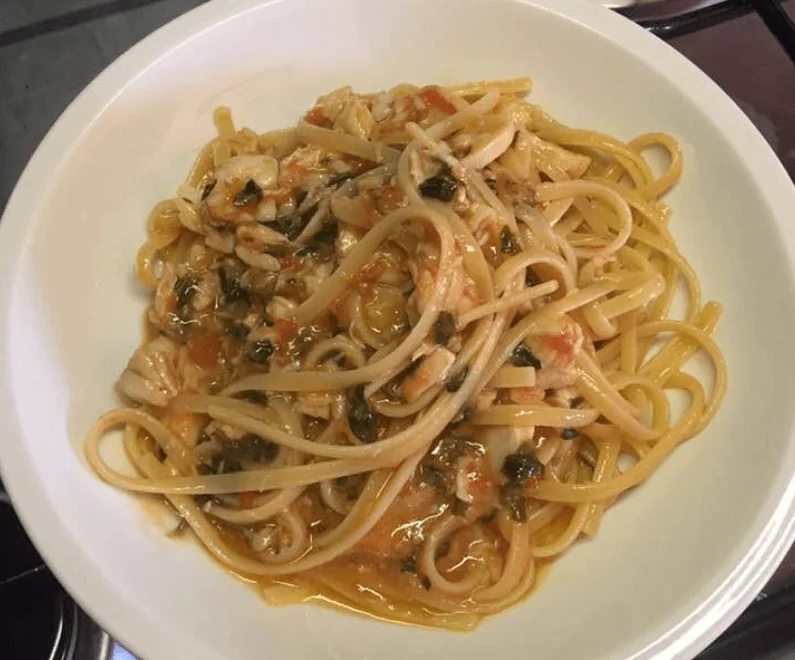 Linguine al filetto di pesce persico con pomodoro e prezzemolo su piatto di ceramica siciliana