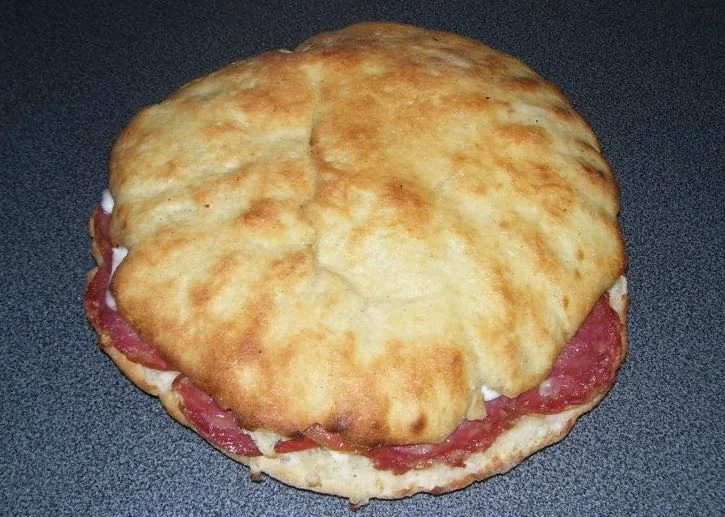 Panino all’ufficiale trapanese con salame e tuma su tagliere di legno, dorato e fragrante