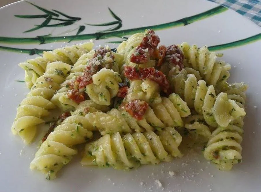 Pasta al pesto di zucchine e pomodori secchi servita con basilico e pecorino