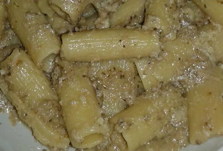 Piatto di pasta col pesto di melanzane alla siciliana decorato con foglie di maggiorana fresca e scaglie di pecorino