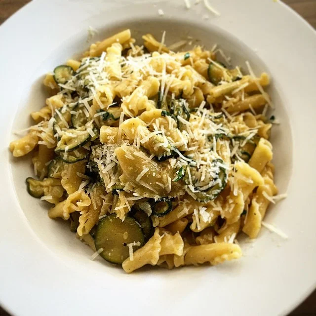 Pasta con le zucchine e pecorino servita in piatto fondo con pepe nero e scaglie di formaggio