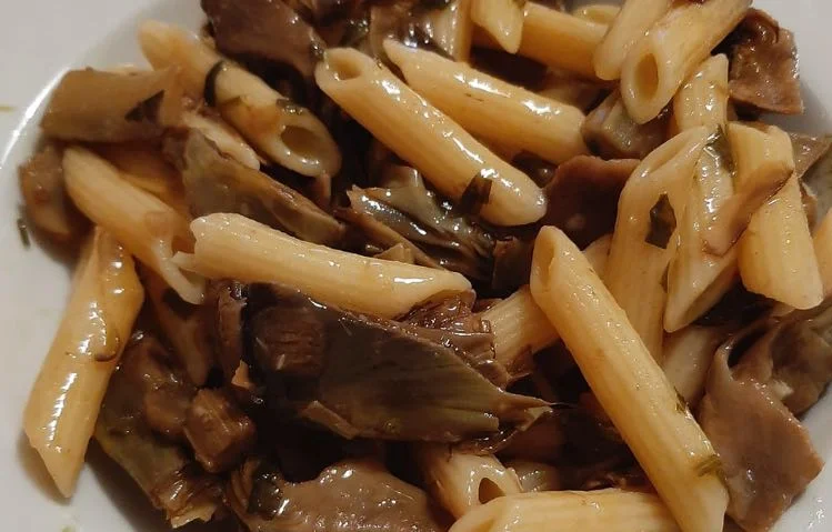 Penne ai carciofi servite in piatto di ceramica siciliana con scaglie di pecorino e pepe nero