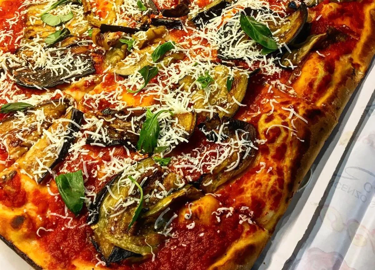 Pizza alla Norma con melanzane fritte, ricotta salata e basilico fresco servita su tagliere in legno