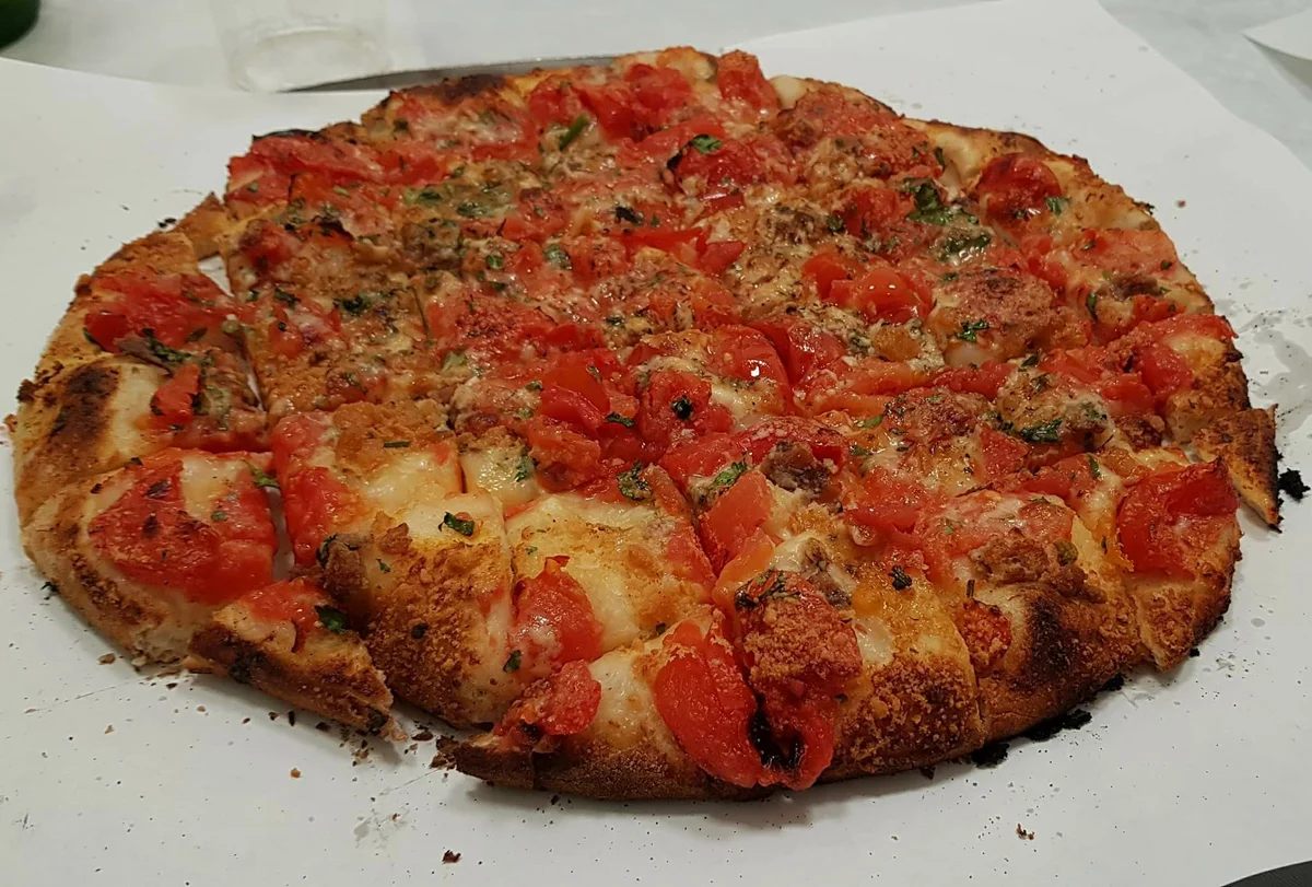 Pizza rianata trapanese con pomodori, acciughe e origano su tavola in legno rustica