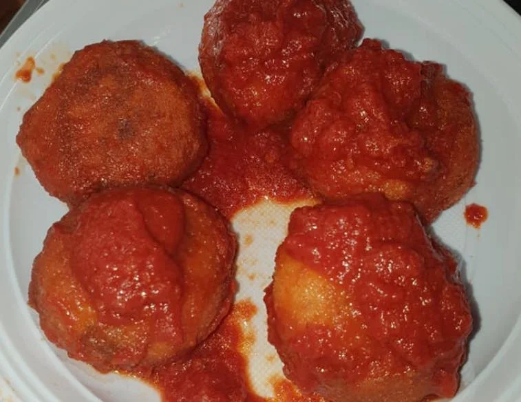 Polpette di pane alla siciliana immerse in salsa di pomodoro, servite su piatto di ceramica siciliana