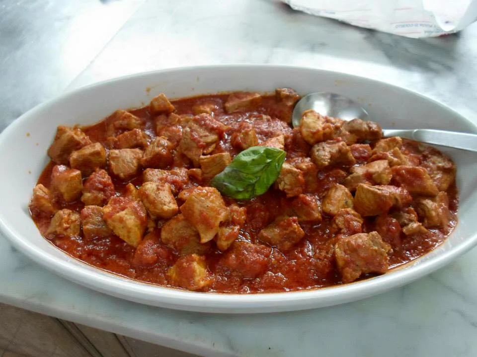 Spezzatino di maiale alla siciliana servito con basilico fresco su piatto in ceramica
