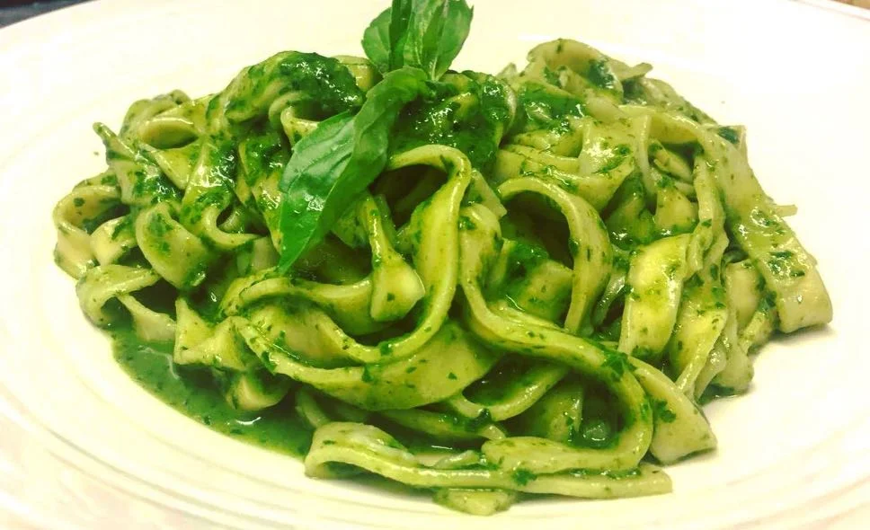 Tagliatelle alla salsa al basilico cremose con mandorle e pecorino su piatto siciliano decorato